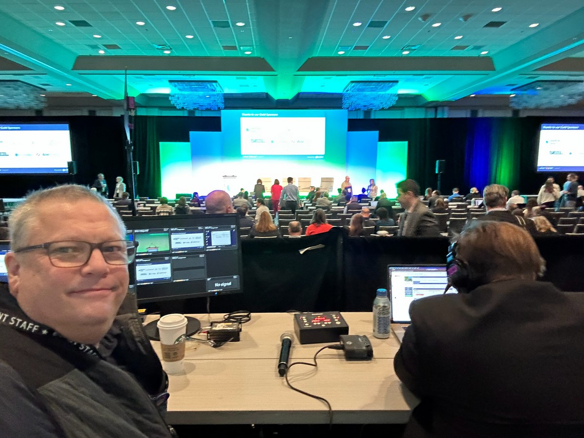 Keith Johnston at the front-of-house production position in a ballroom, with monitors and a general session stage in the background