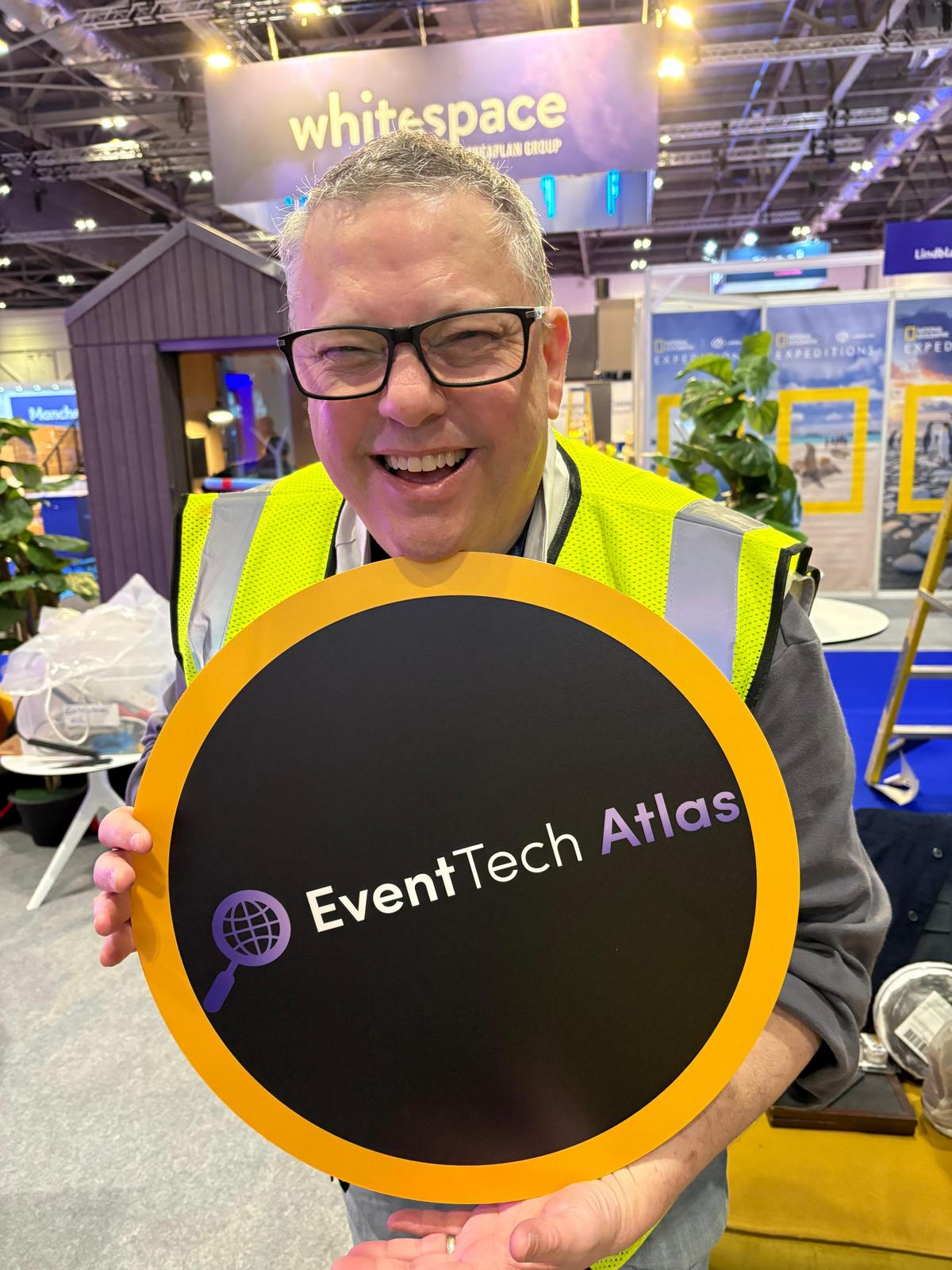 Keith Johnston on a trade show floor holding a round Event Tech Atlas sign